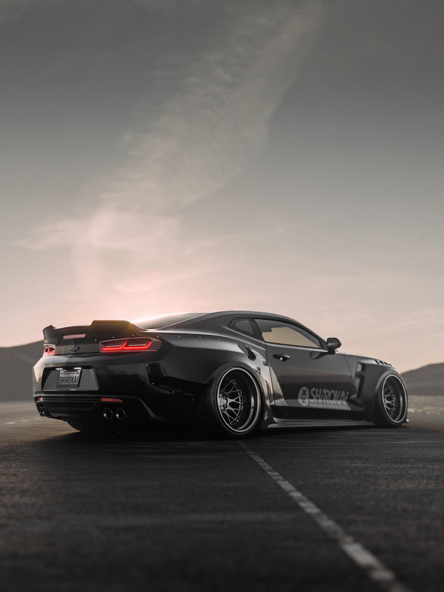 Black Chevrolet Camaro 6th gen widebody kit SHIROKAI Stance lowered Chevy parked on asphalt at sunset