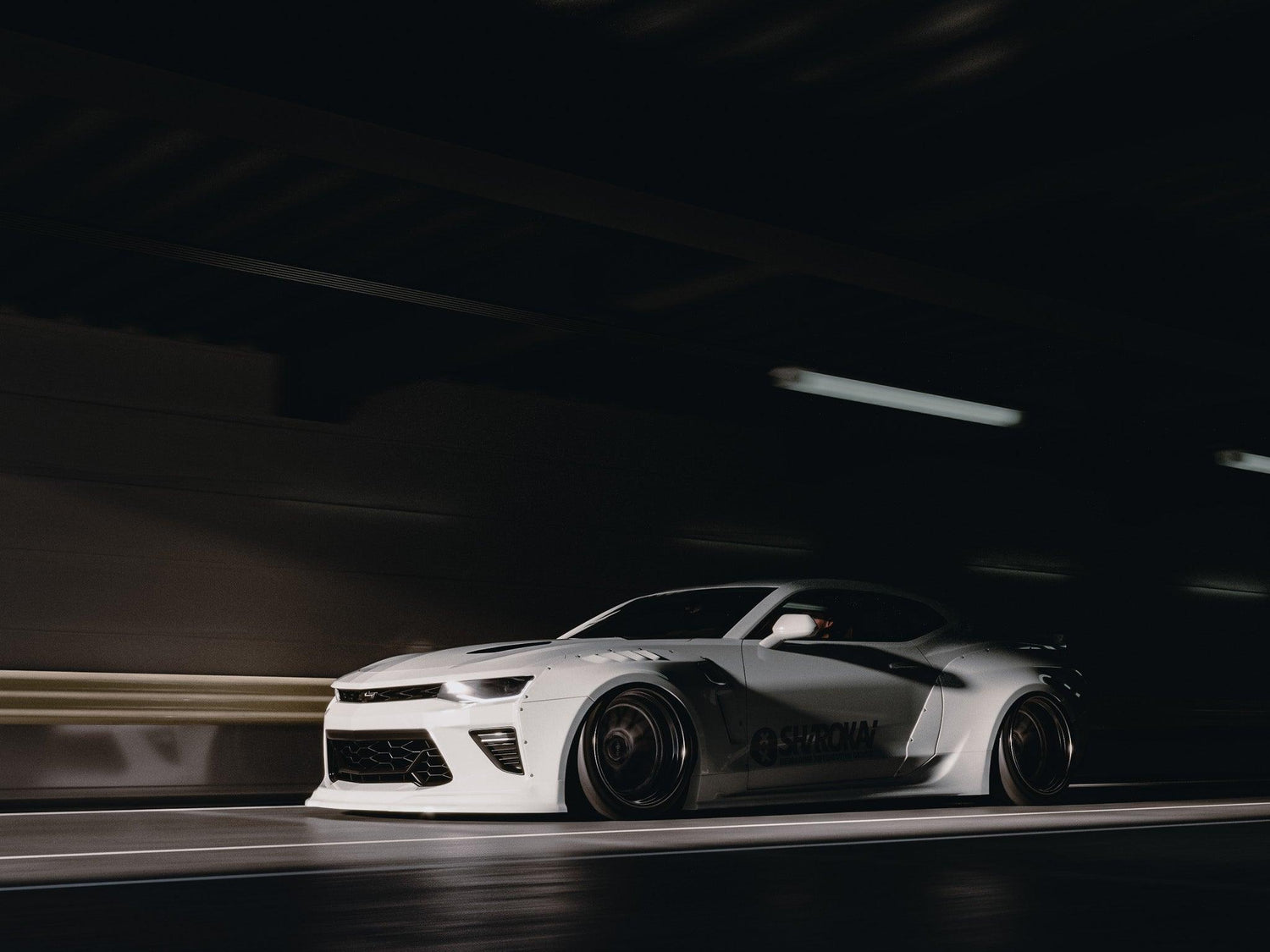 White Chevrolet Camaro 6th gen widebody kit SHIROKAI Stance lowered Chevy driving in dark tunnel