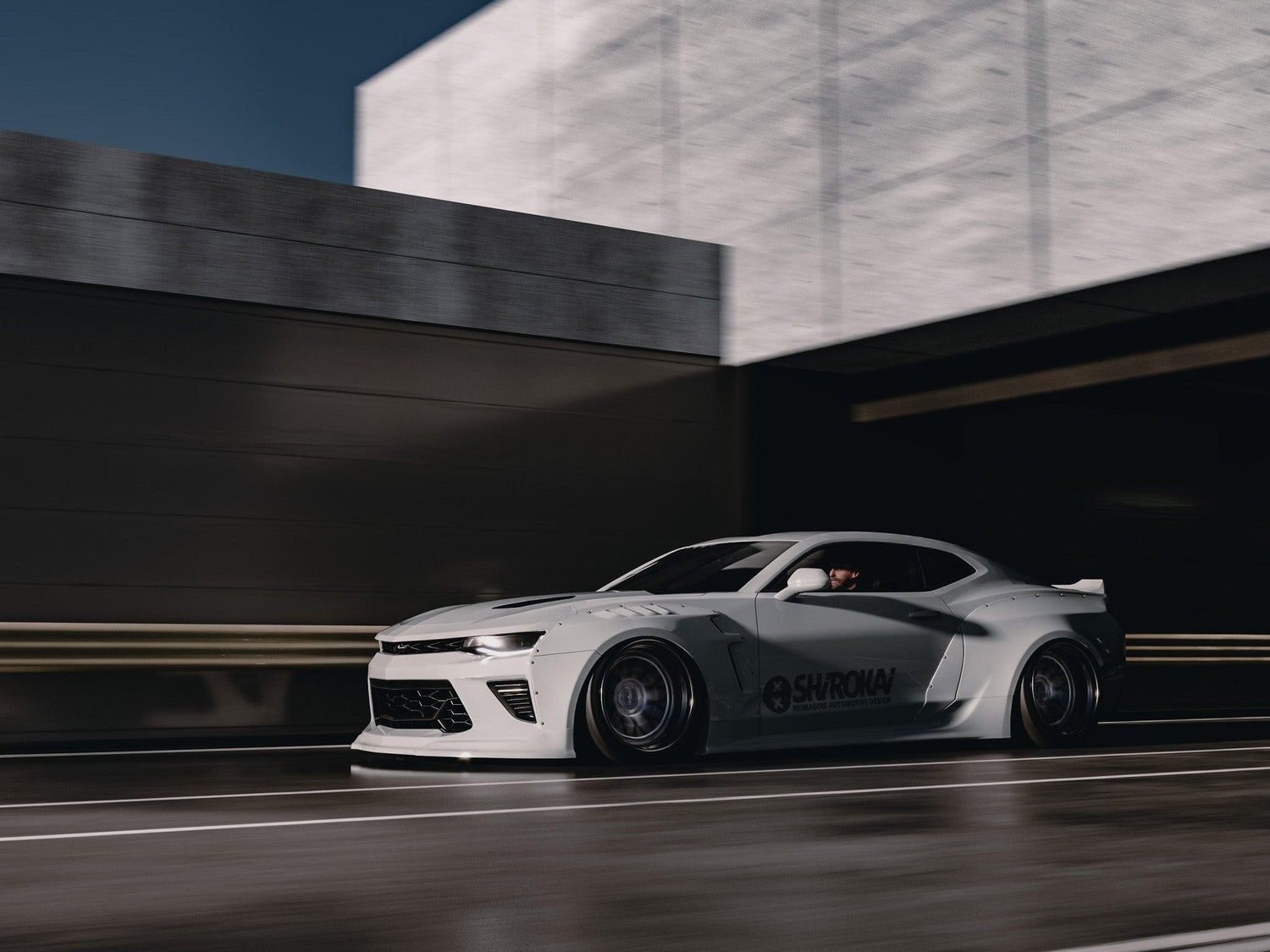 White Chevrolet Camaro 6th gen widebody kit SHIROKAI Stance lowered Chevy driving on road near concrete building