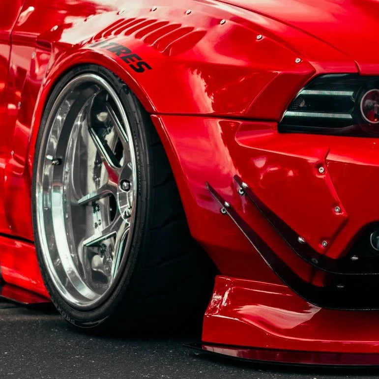 Close-up of red sports car front wheel with polished rims and wide body kit on asphalt