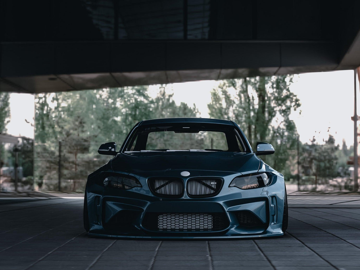 Front view of a BMW M2 2015-2018 widebody kit SHIROKAI installed on a dark blue car parked under a bridge