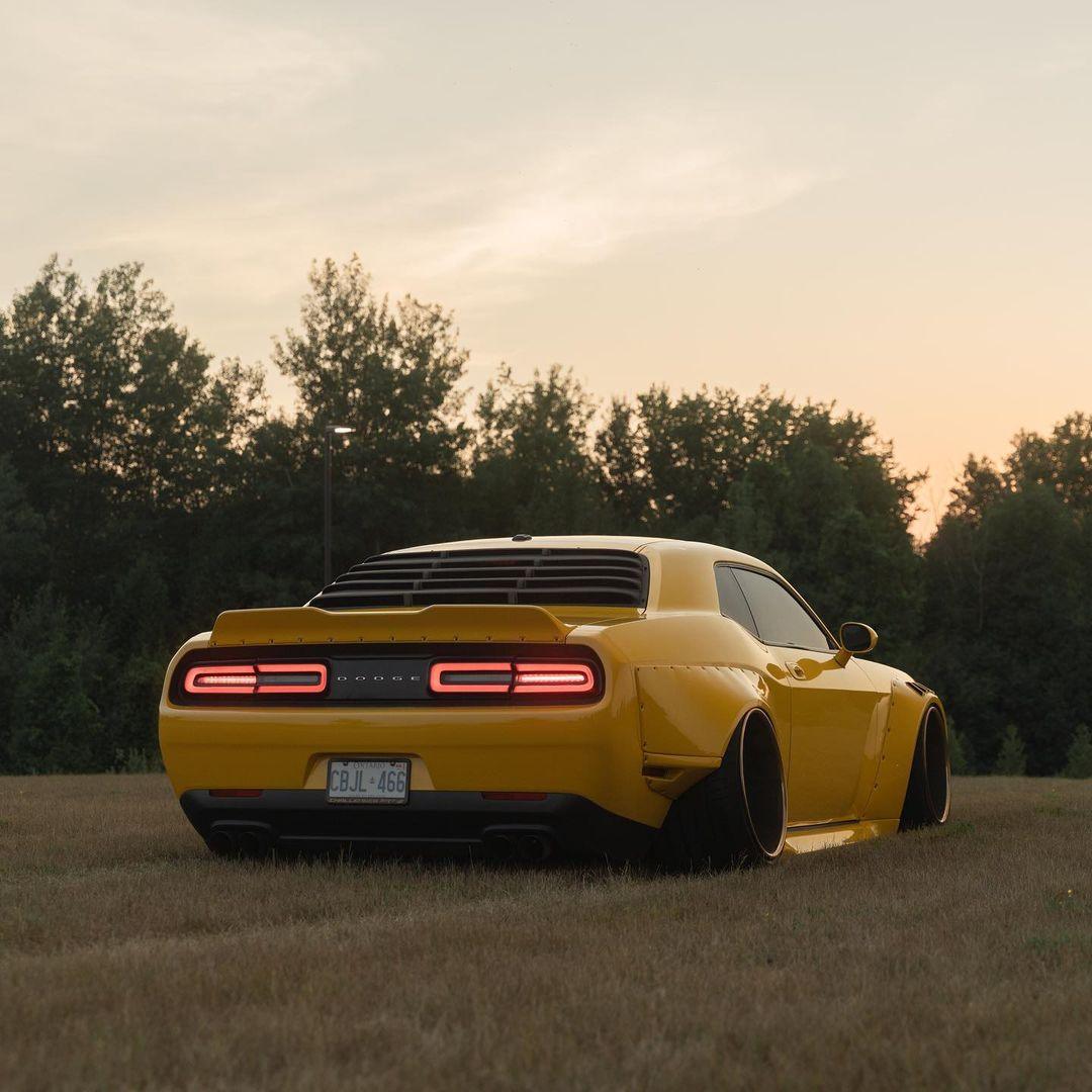 Yellow Dodge Challenger HELLCAT SHIROKAI widebody kit with aggressive rear fenders and custom wheels on grass