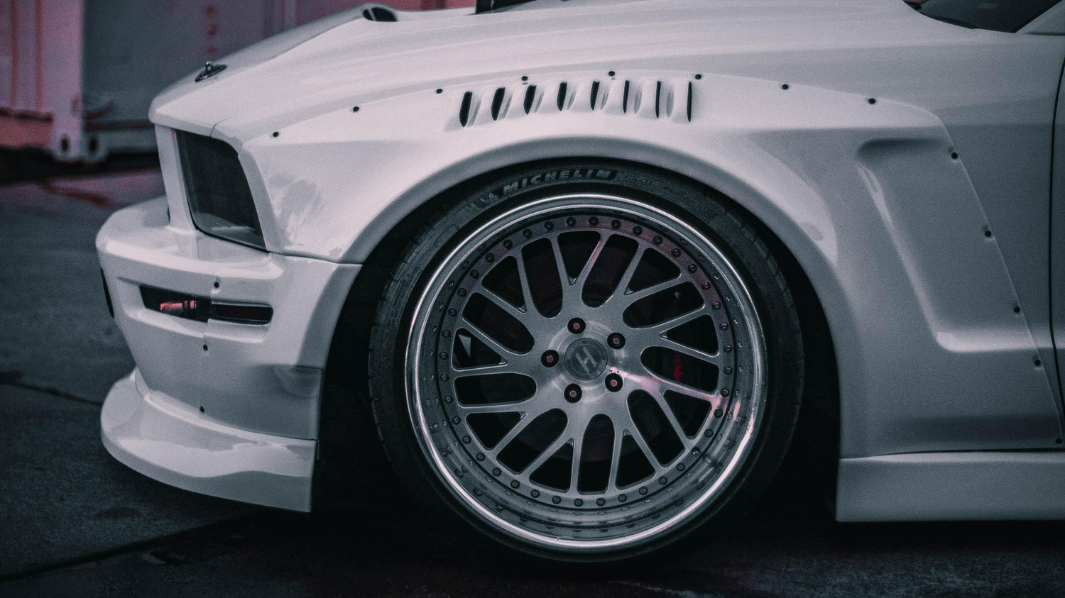 Close-up of a white Ford Mustang S197 with SHIROKAI widebody kit showcasing custom fender and wheel