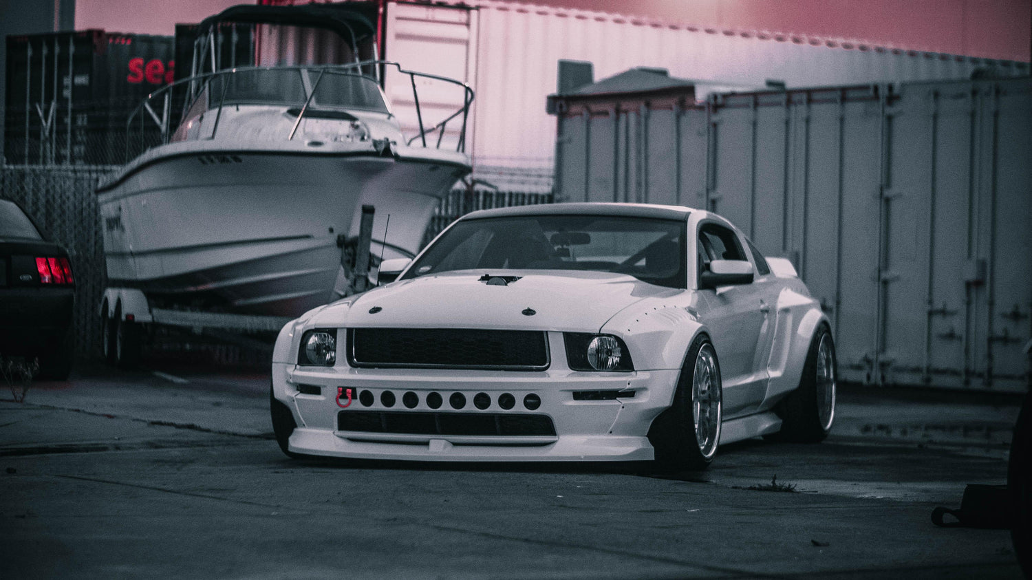 White Ford Mustang S197 with widebody kit SHIROKAI installed parked near boats and shipping containers