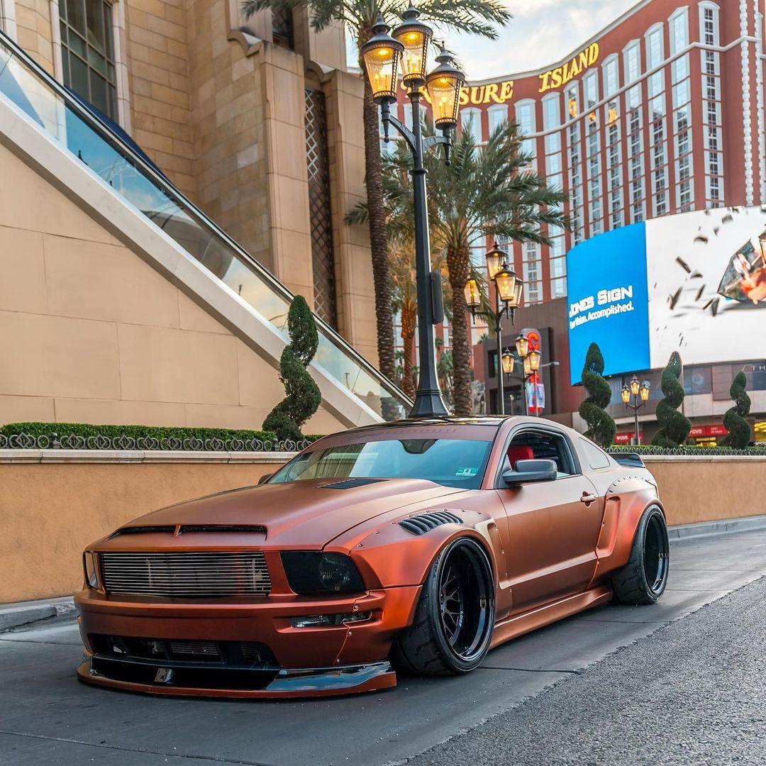 Ford Mustang S197 widebody kit SHIROKAI in matte orange with black wheels parked on city street