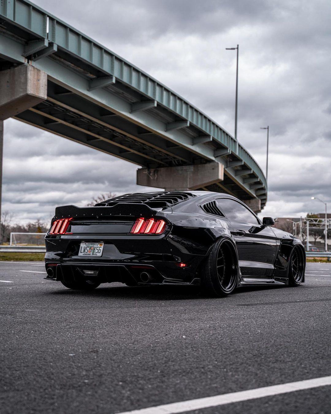 Black Ford Mustang S550 with SHIROKAI widebody kit parked under bridge on cloudy day