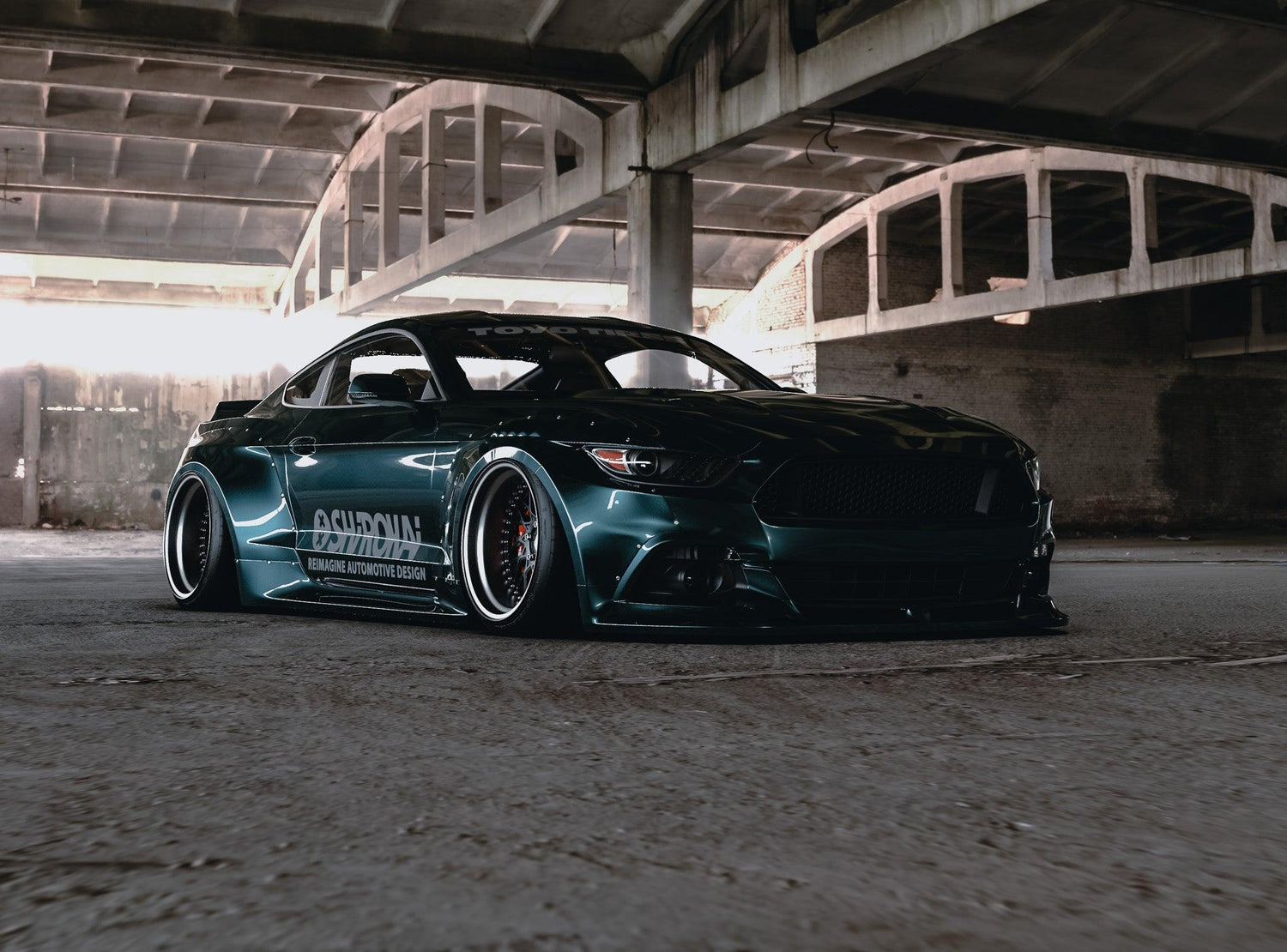 Dark green Ford Mustang S550 with SHIROKAI widebody kit parked under a concrete bridge