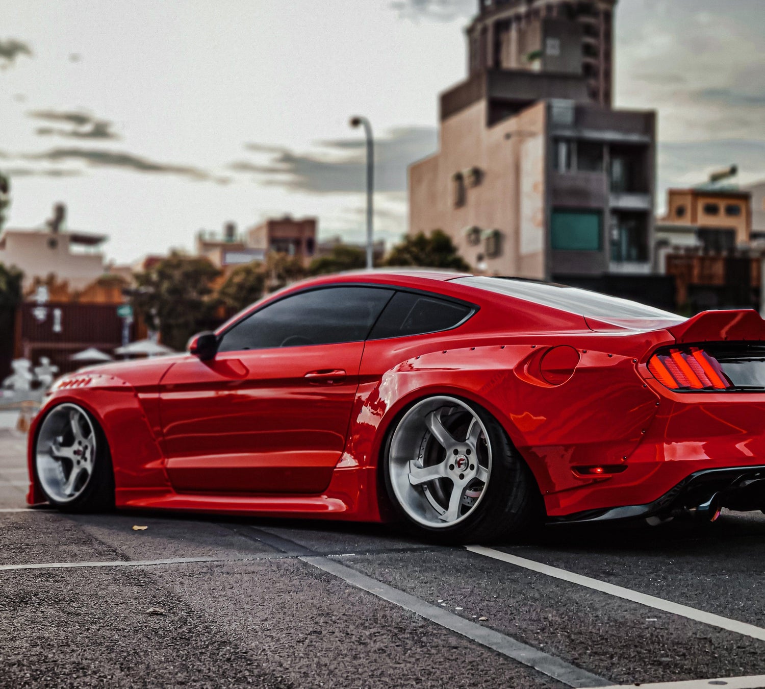 Red Ford Mustang S550 with SHIROKAI widebody kit parked on urban street at sunset